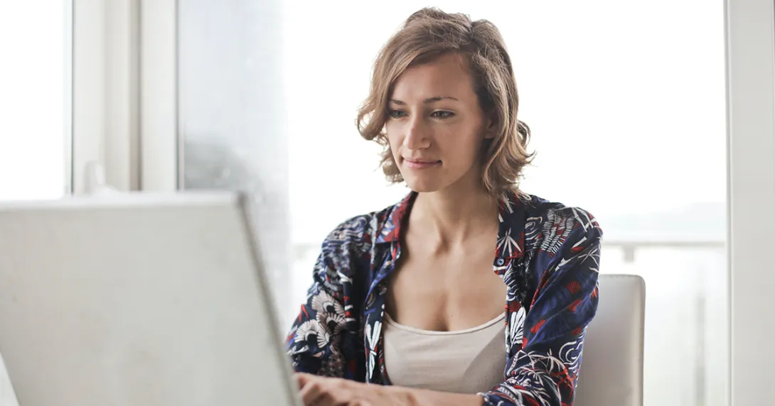 Woman sits at a table and is reading and typing on a laptop
