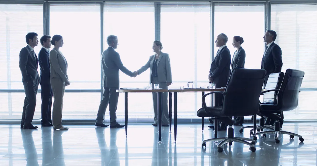 Individuals stand in a lobby while two shake hands.
