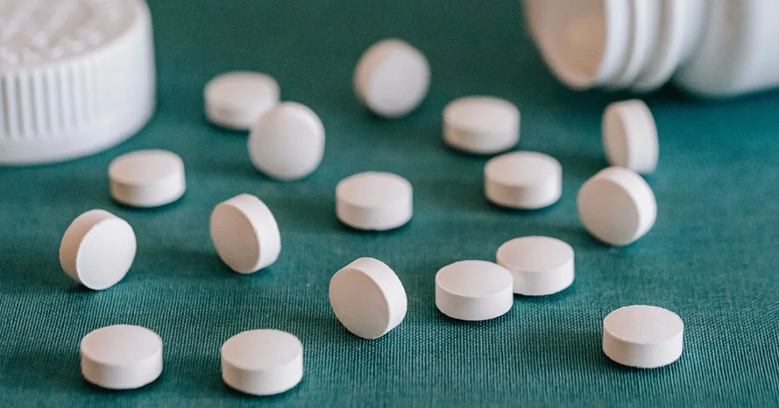Pills lay on a surface with an open prescription bottle in the background