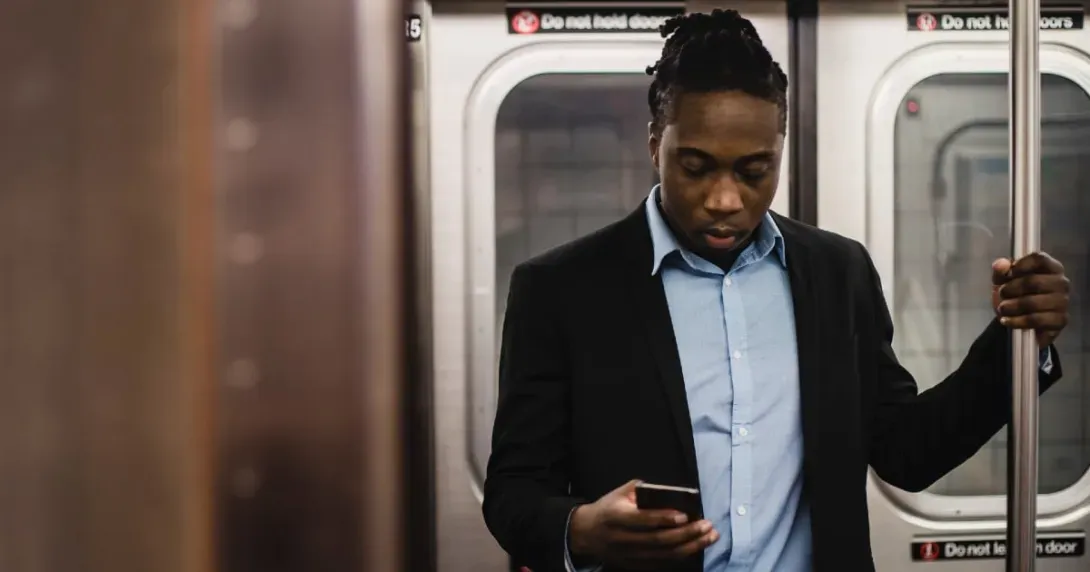 Man in shirt and blazer using his phone while standing in a subway car