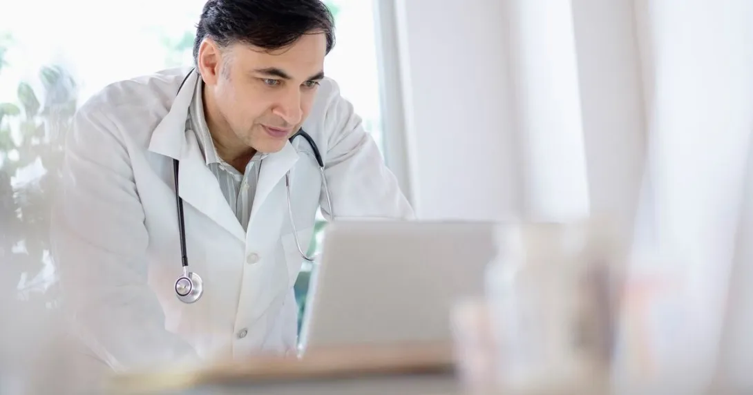 A doctor looking over a patient's medical record on a laptop