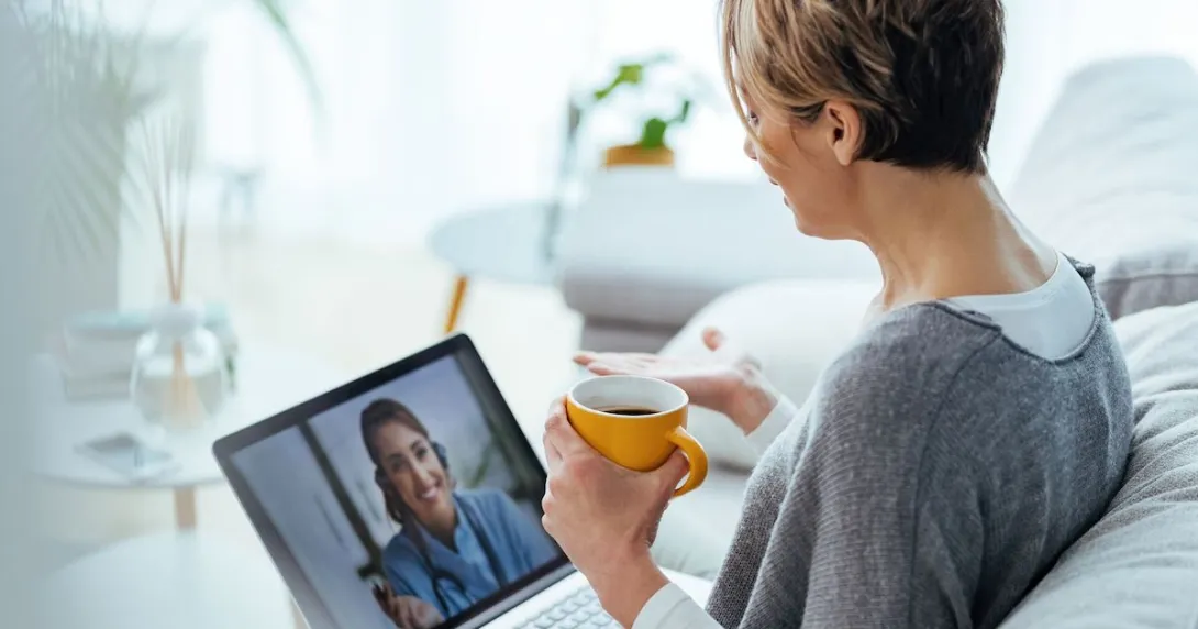 A patient holding a cup of coffee in a virtual call with their doctor