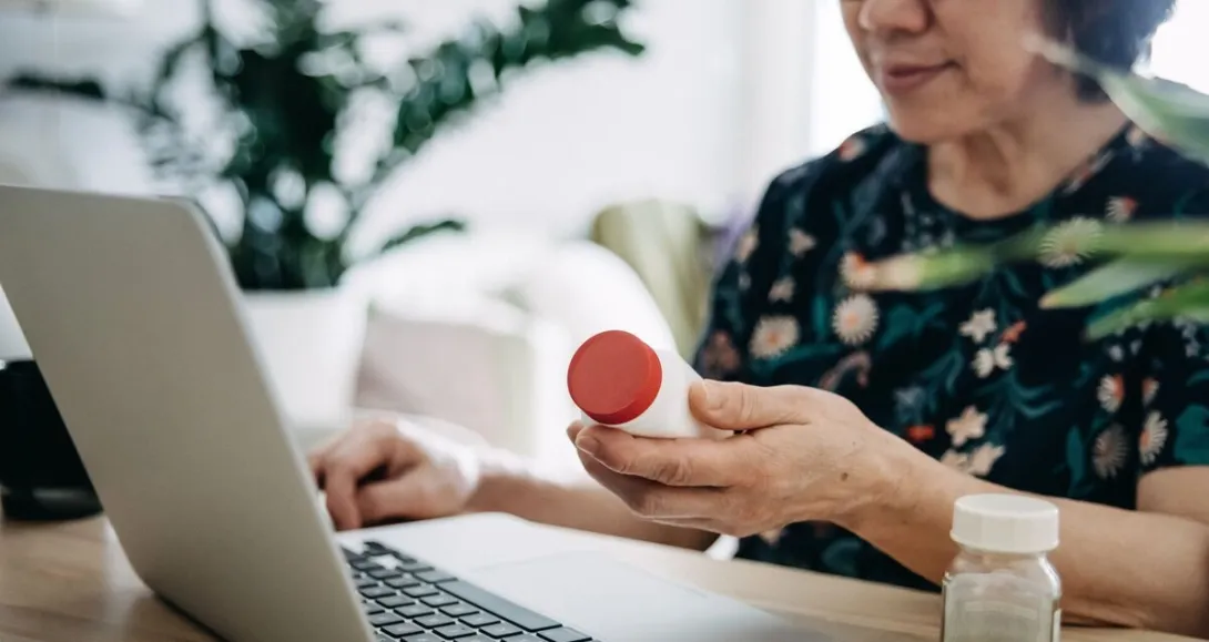 A patient holding a bottle of medicine is in a virtual consultation with a doctor using laptop