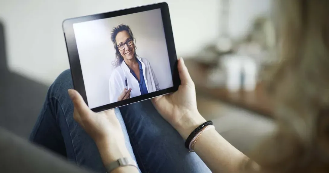 Patient holds a tablet in a telehealth call with her doctor