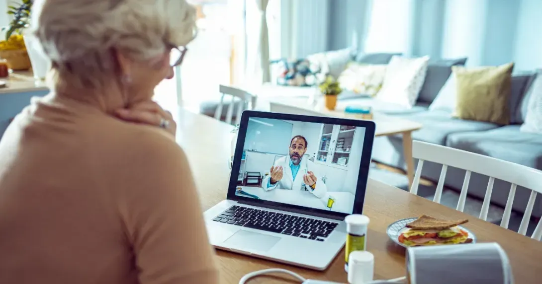 senior woman speaks to her doctor on a laptop at her kitchen table