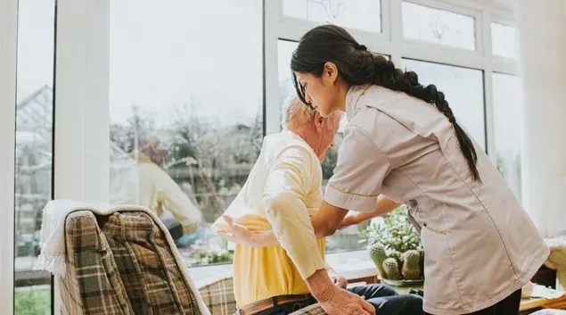 Nurse helps a senior patient stand up from a recliner