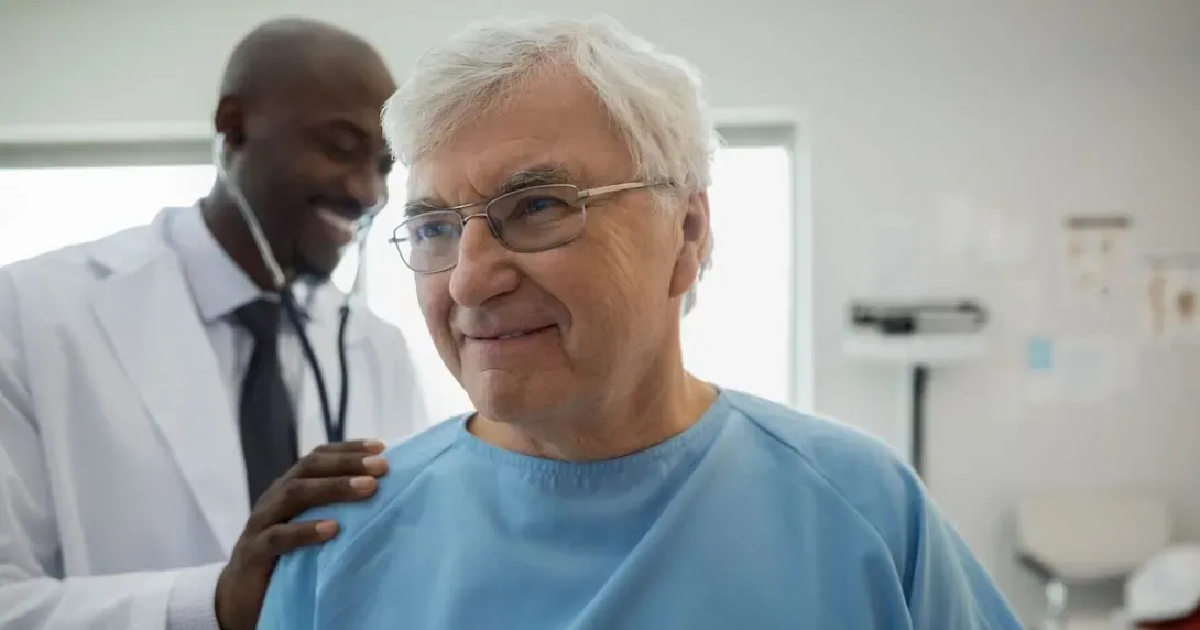 Doctor listens to older male patient's heart with stethoscope 
