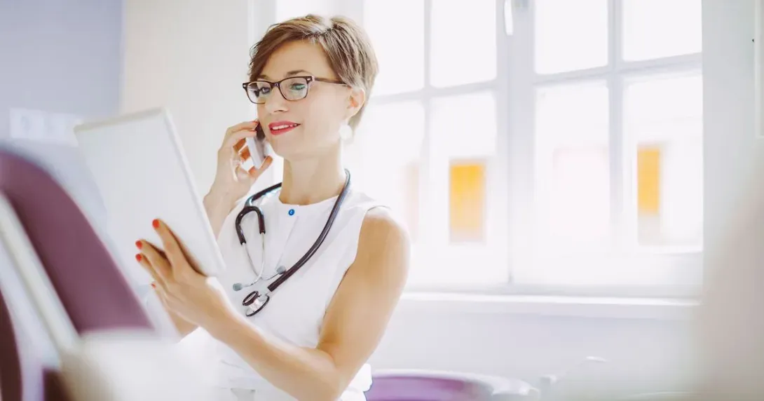 Female doctor reviews information on a tablet while speaking on a mobile device