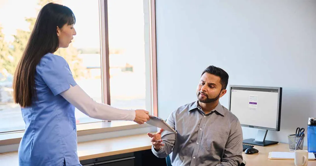 Healthcare worker hading tablet to person at a desk