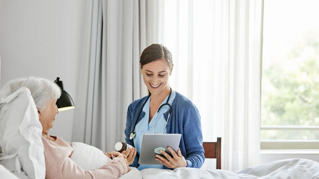 A caregiver holding a digital tablet and checking an elderly patient's medication