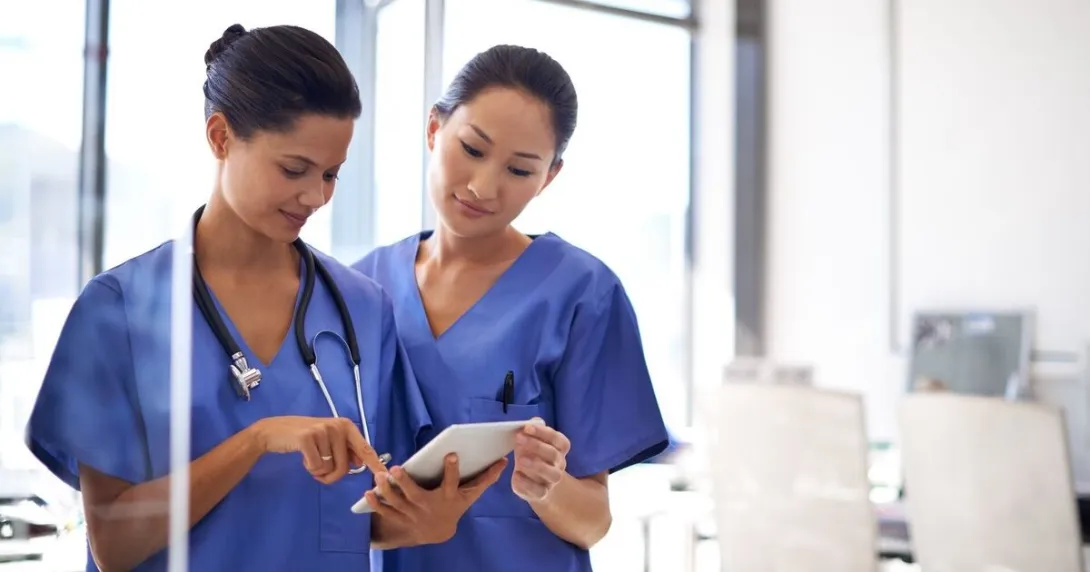 Two nurses checking a patient file on a digital tablet