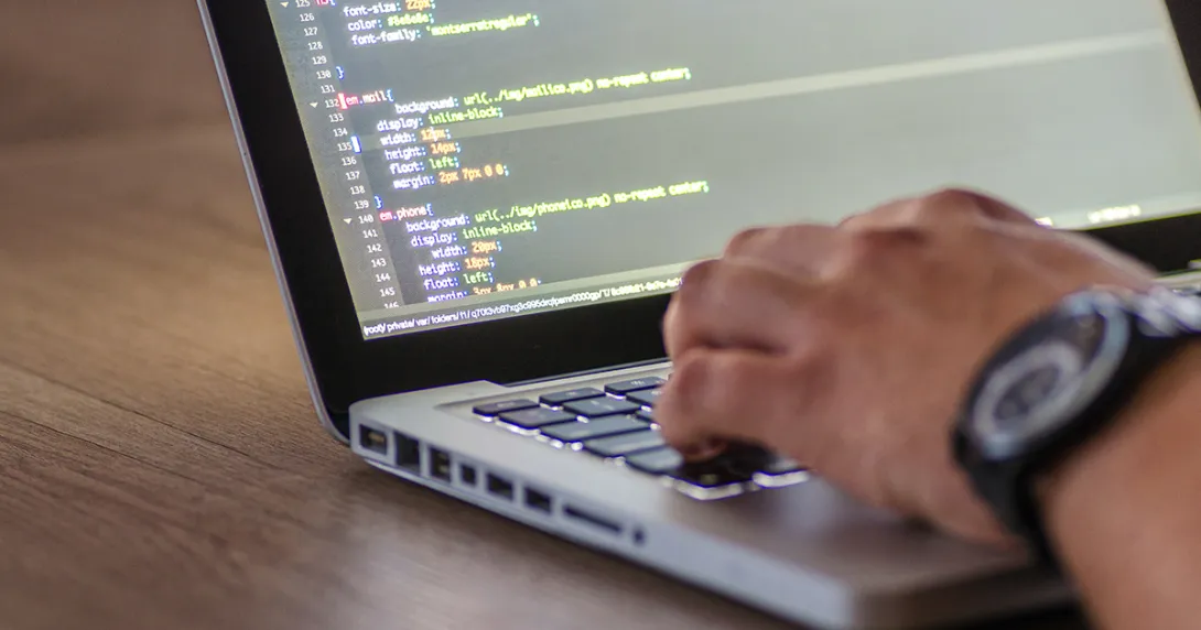 Close-up of a software developer's hand on a laptop with code on the screen