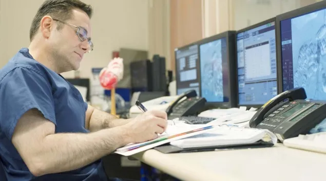 Healthcare worker taking notes in front of computer monitors