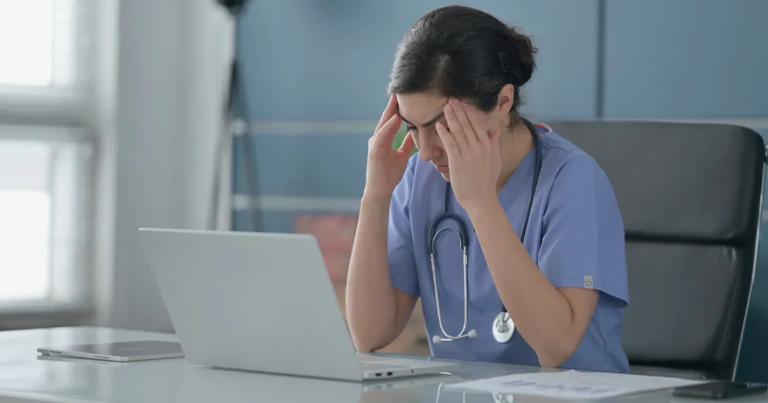 Nurse sitting in front of laptop with hands to head