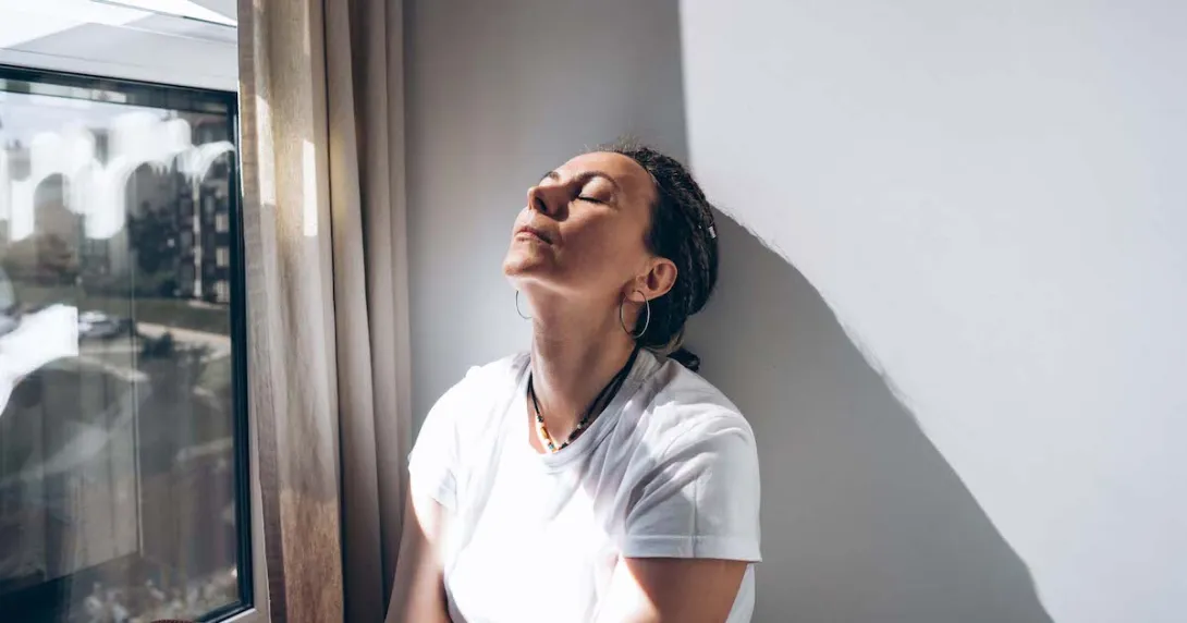 Woman stands by window head against a wall