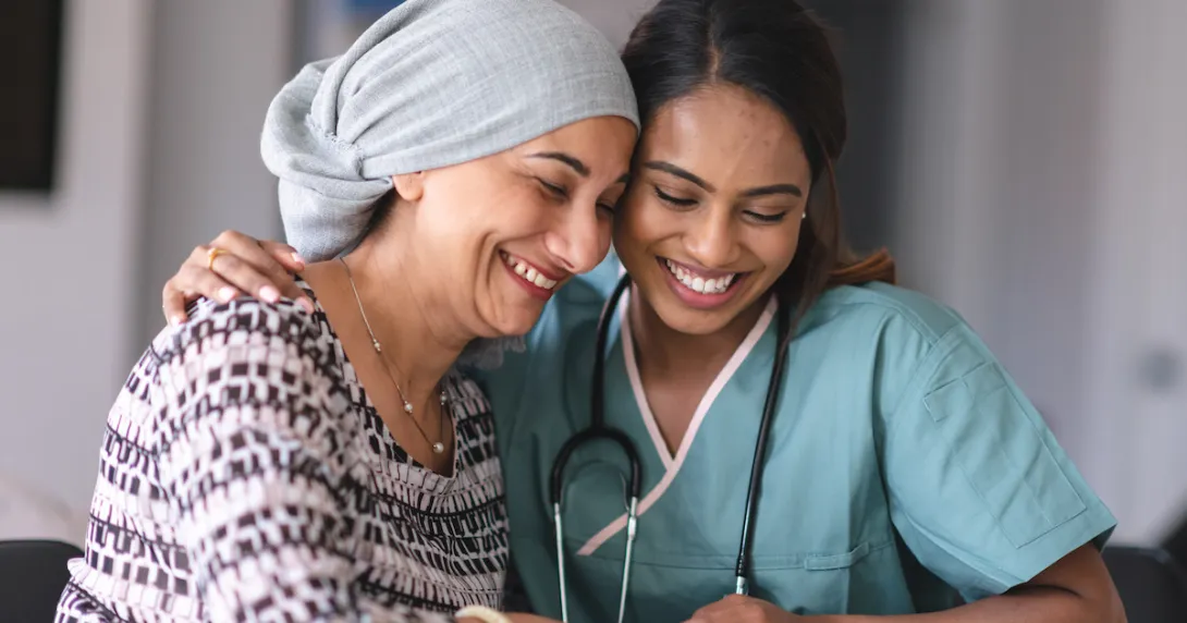 A clinician and a cancer patient with a head scarf smile as they look down.