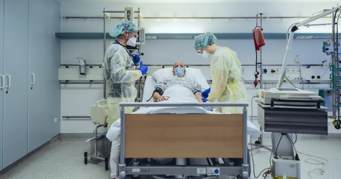Two staff treating an ICU patient in bed
