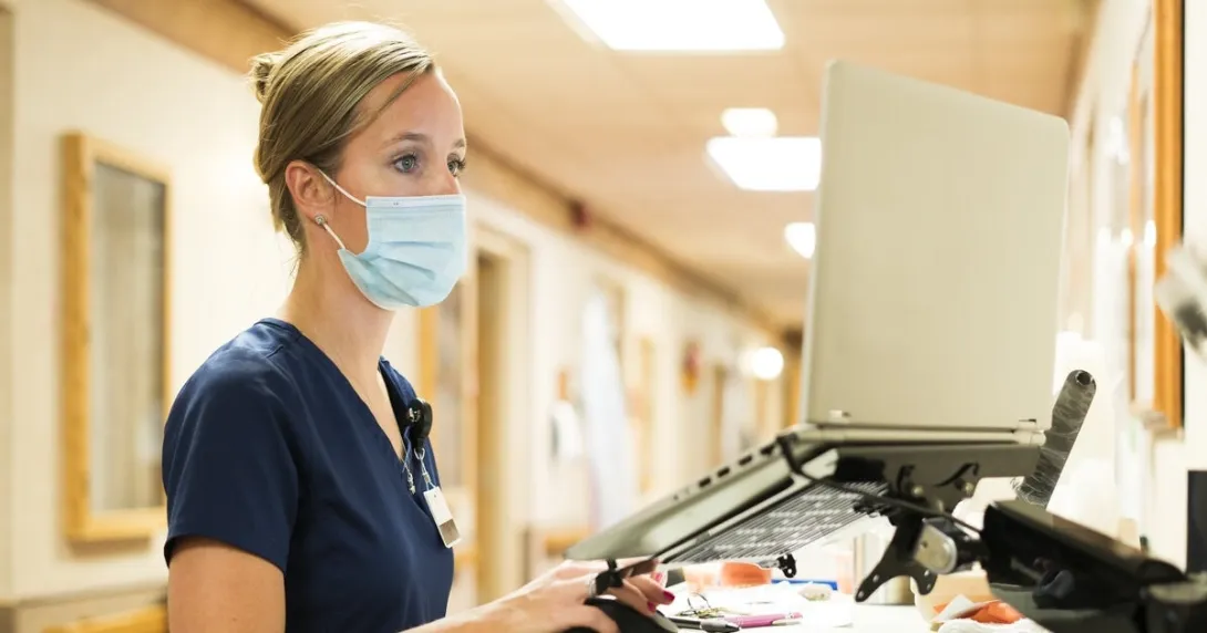 A nurse checking on a patient's file in a hallway laptop