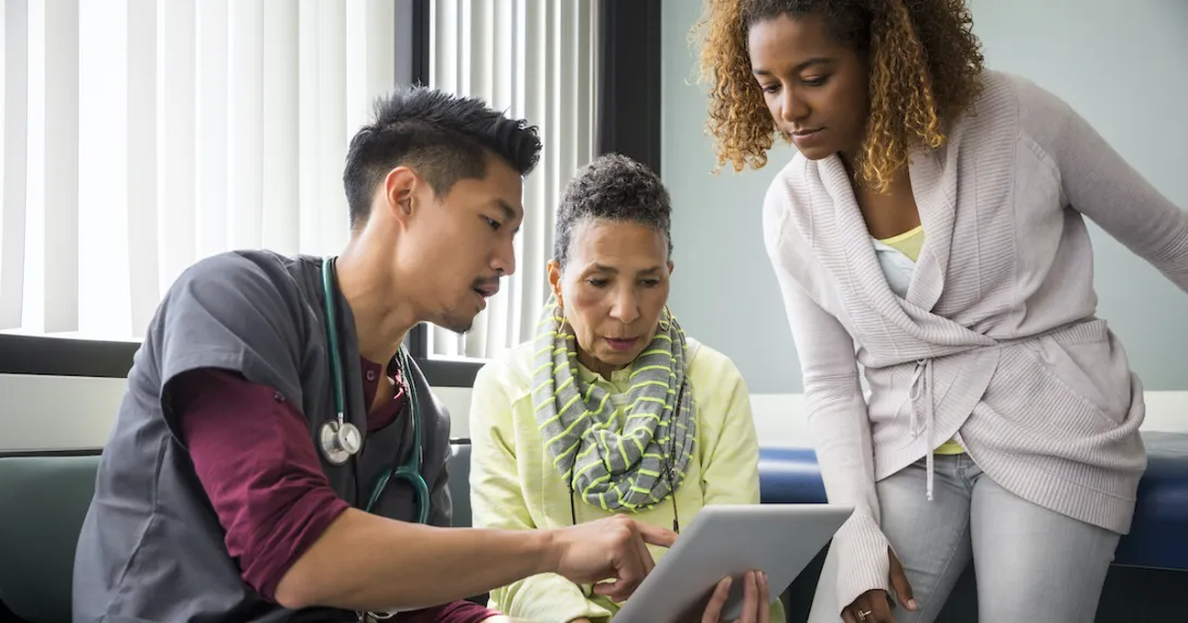 A doctor explaining to a patient and their carer their diagnosis using a digital tablet