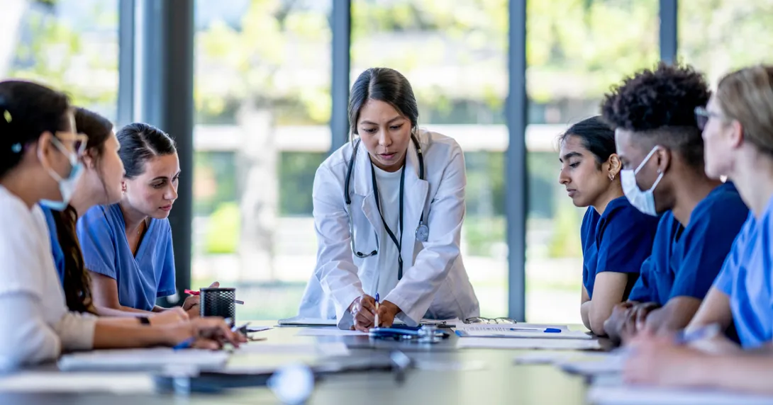 Doctor pointing out item on table to group of sitting healthcare workers