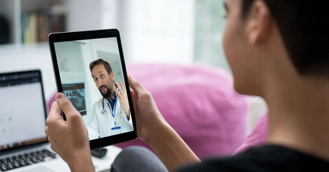 A doctor appears on a tablet having a telehealth visit with a person with short hair.