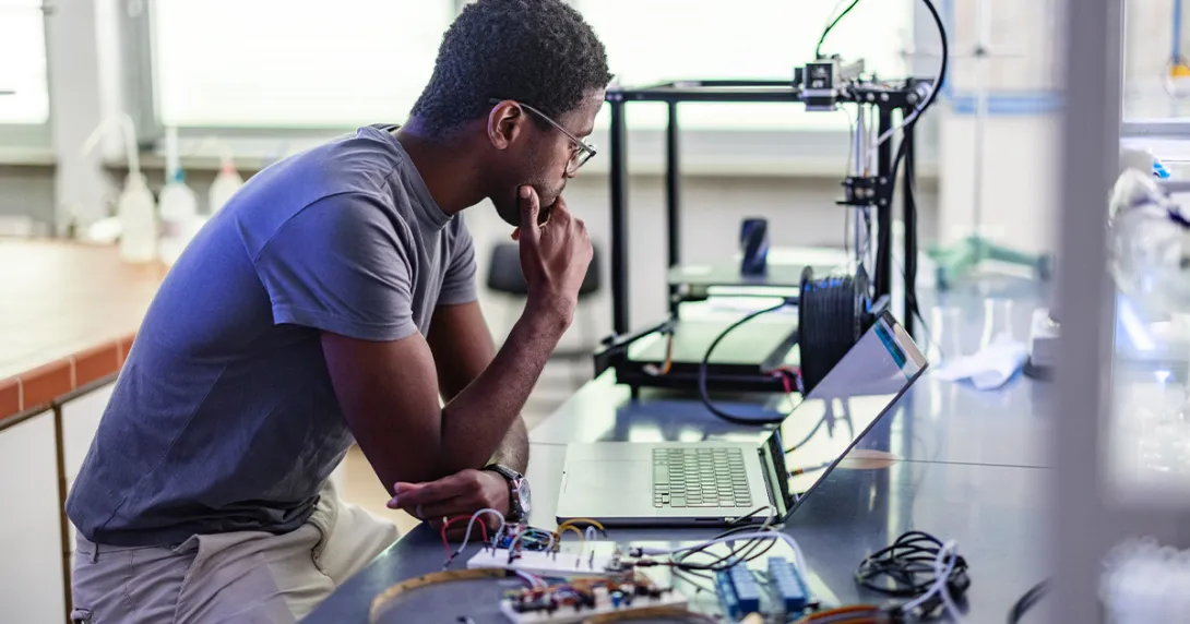Worker looking at laptop surrounded by electronic components