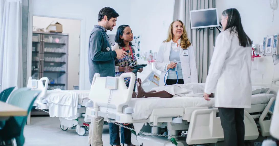 group of healthcare workers talking over hospital bed