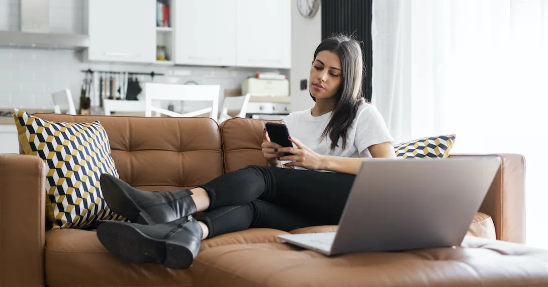 Woman on a couch at home checks her phone to book a doctor's appointment.