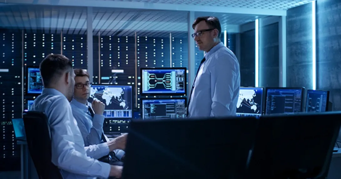 Three cybersecurity professionals talk in a network control room.