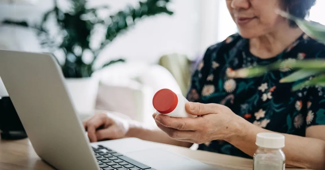 Person holding pill bottle using a laptop