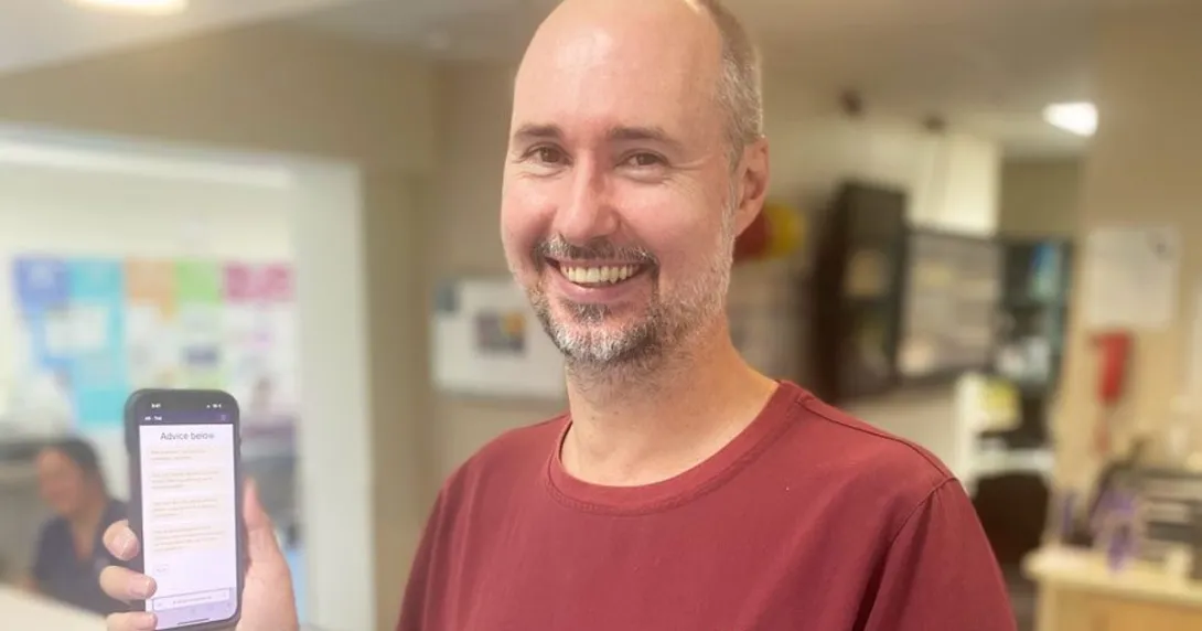 Dr Eamonn Eeles holding a mobile phone showing the electronic tool for assessing delirium causes