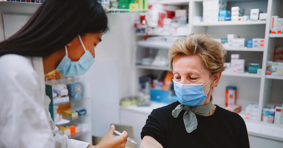 A pharmacist at a retail pharmacy delivers a vaccine to an older woman.