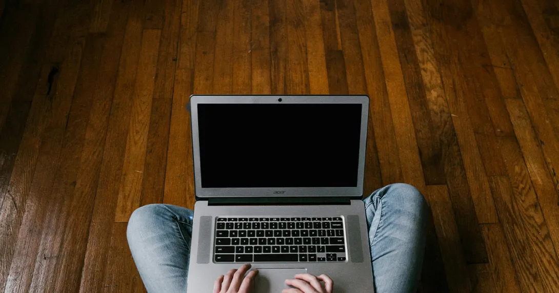 Laptop on a mans lap sitting on an oak wood floor
