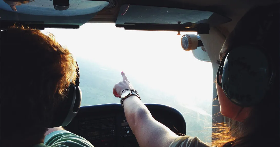 In a plane, a copilot points to a destination on the horizon.
