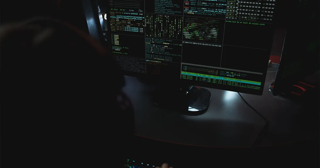 A shadowed figure views a computer terminal monitoring data streams.