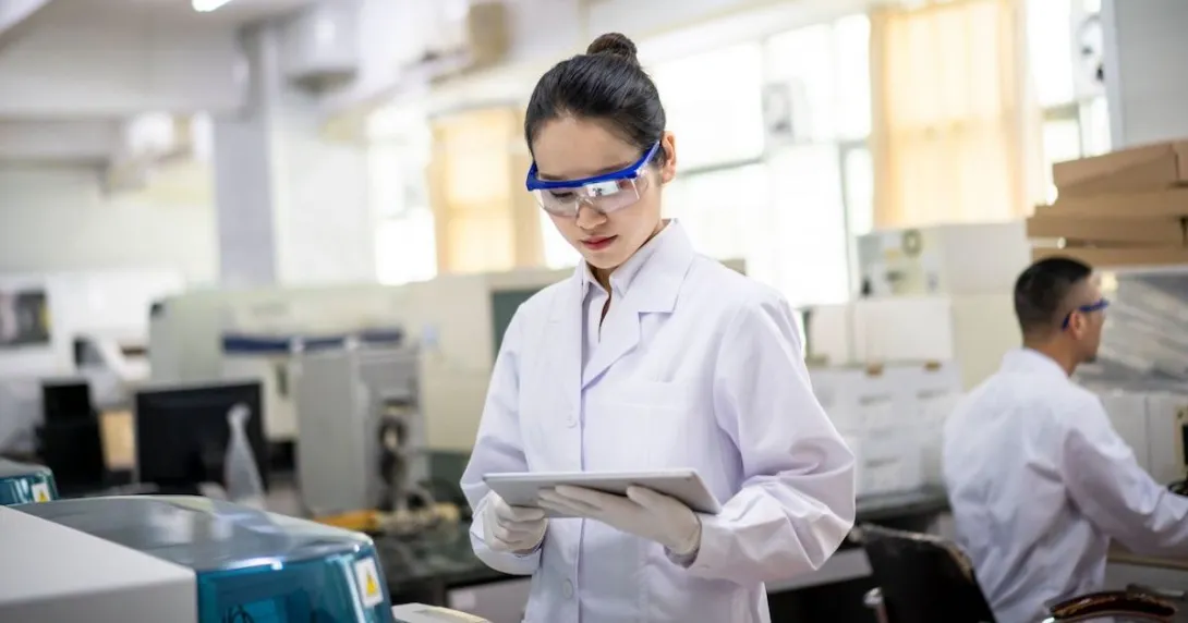 A female healthcare researcher in a lab looks at a tablet.