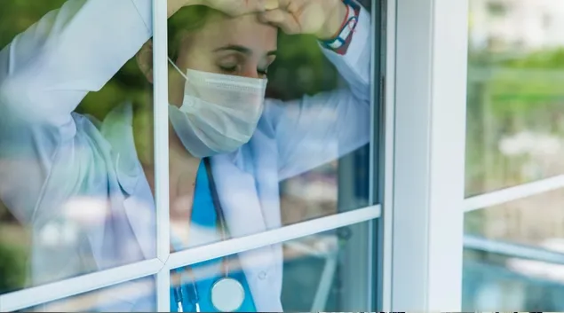 Exhausted health worker leans on window