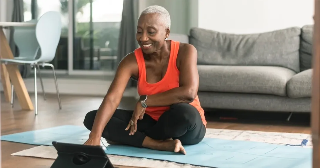 Woman sits on yoga mat in living room looking through data on her tablet