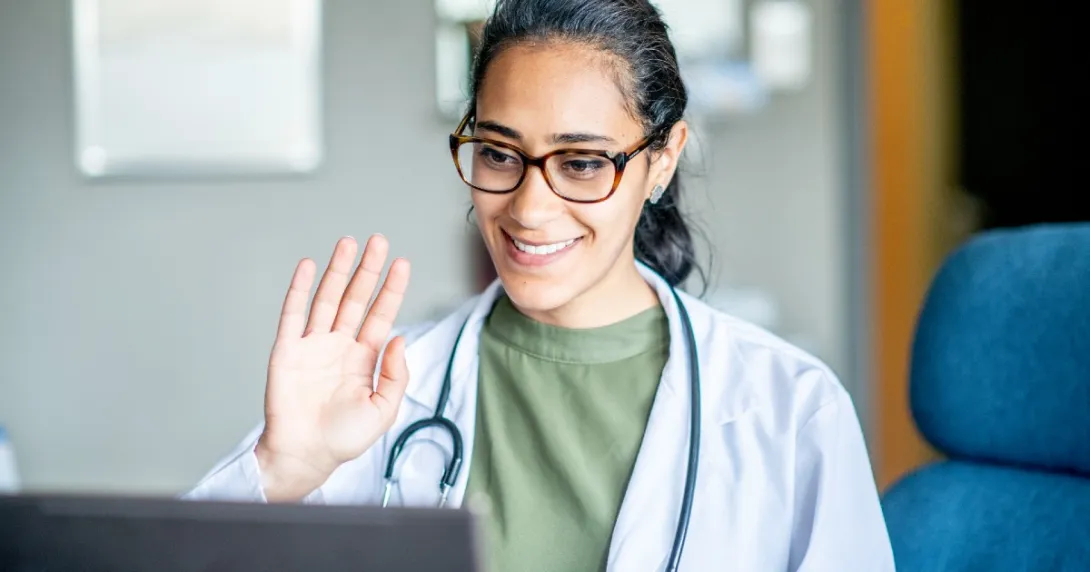 Doctor smiles and waves into a laptop during a telehealth visit