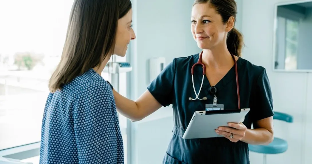 A nurse holding a digital tablet is conversing with a patient