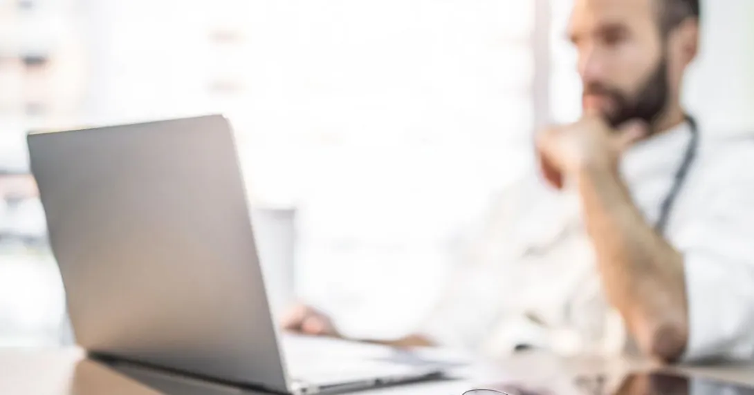 Doctor at desk sits back and reads information on a laptop