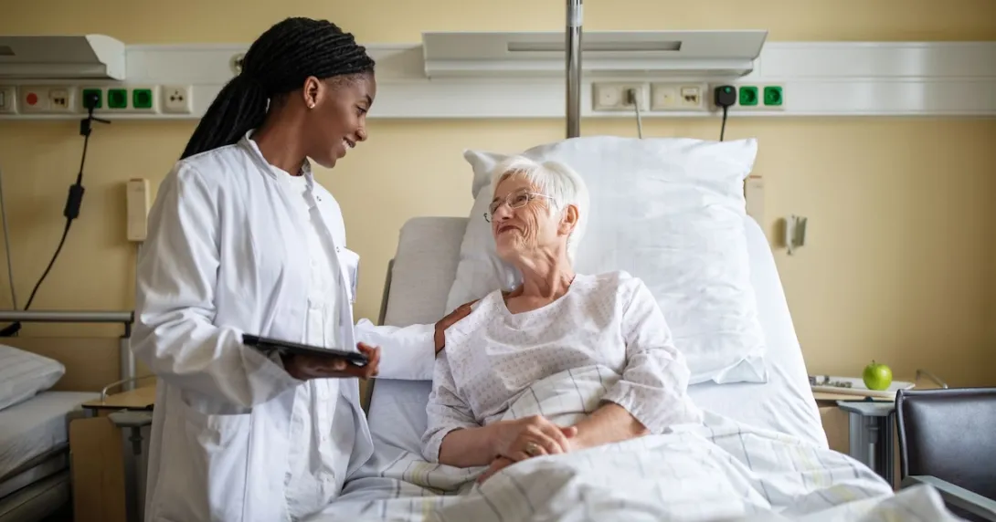A doctor holding a digital tablet interacting with a senior patient in bed.