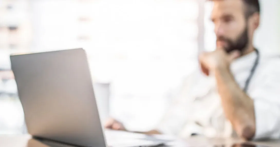 A doctor reviewing a patient file on their laptop