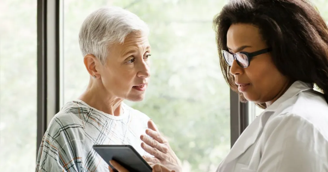 A senior patient consulting with a doctor who is holding a digital tablet