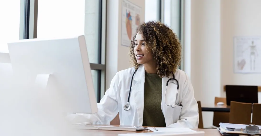 A doctor reviewing a patient's file on a desktop computer