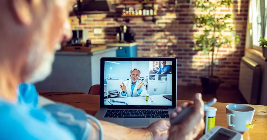 A senior patient is using a blood pressure monitor while consulting with a doctor.
