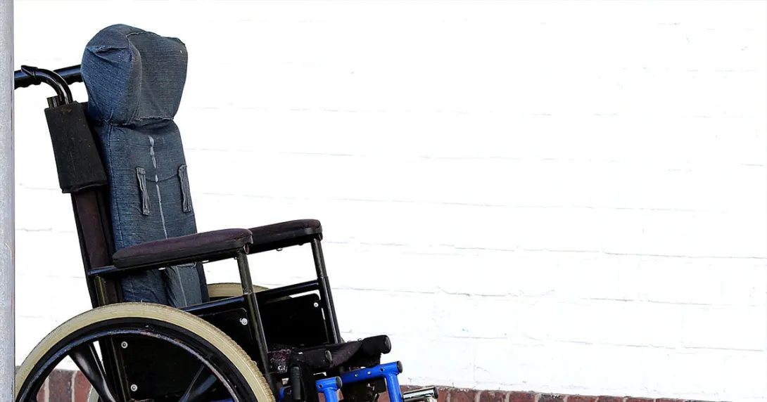 A wheelchair, perhaps for an ALS patient, sits vacant by a wall.
