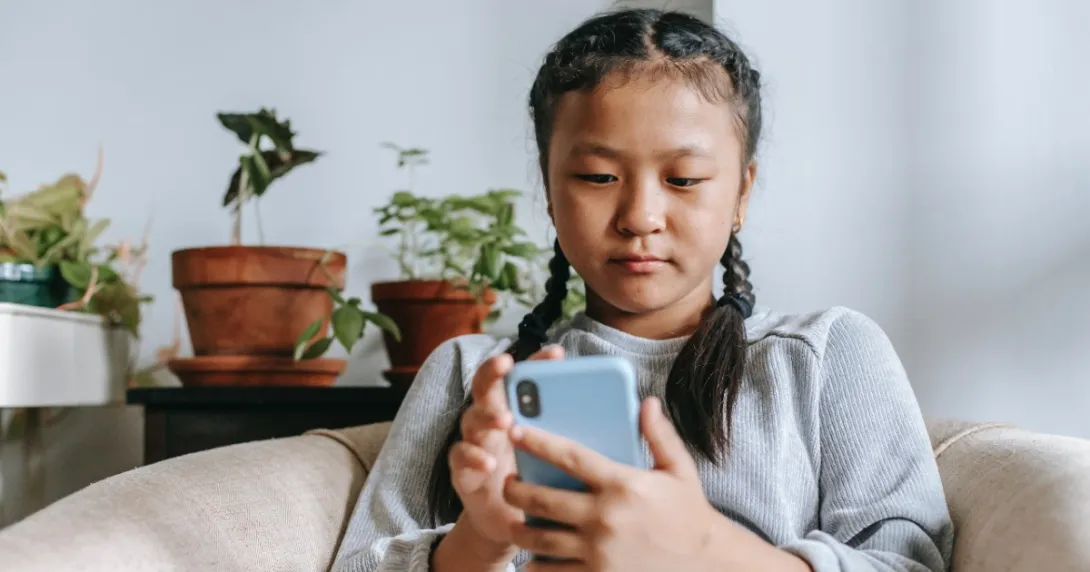 Young person sits on a couch and types on a mobile phone